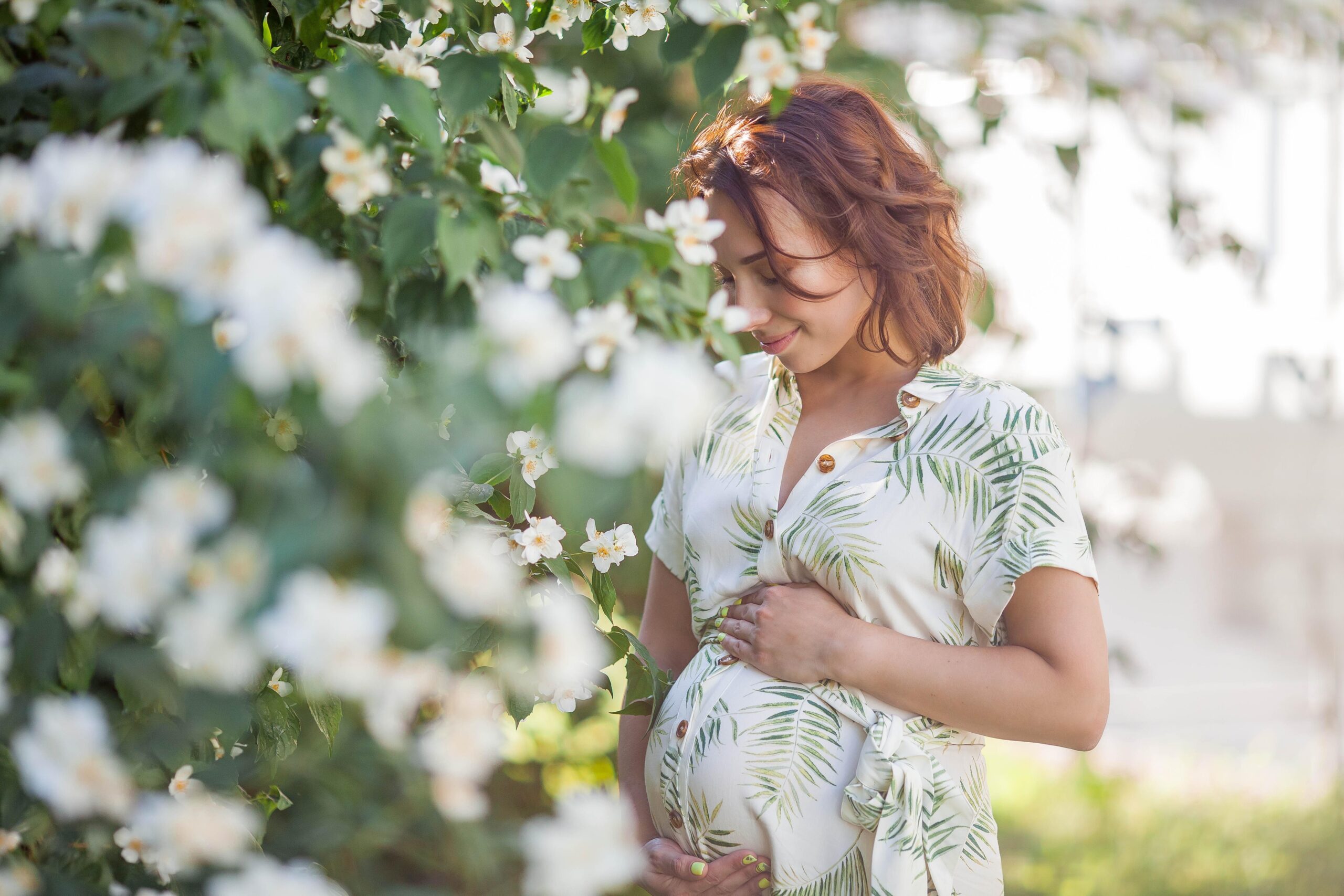 Beautiful young happy pregnant woman is standing near the blossoming tree. Motherhood. Love. Spring.