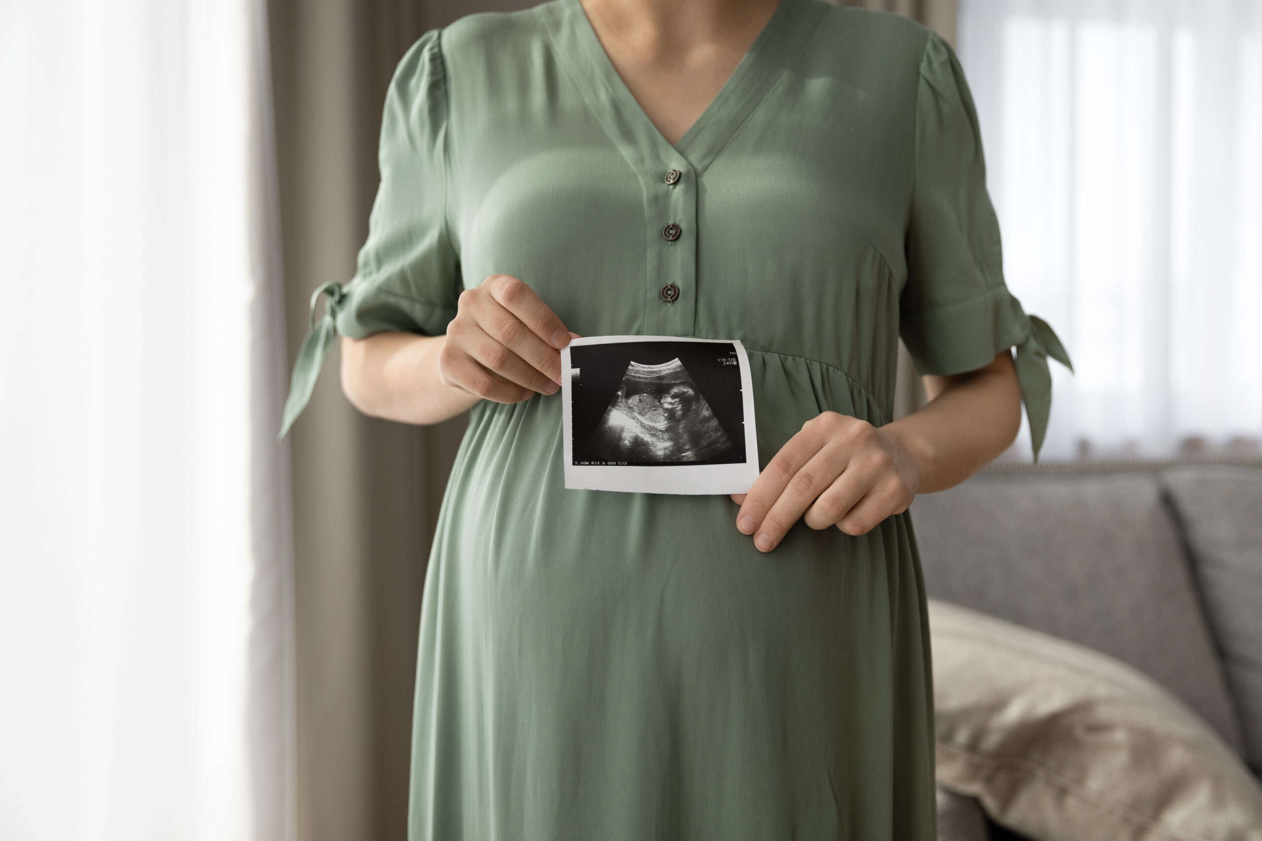 Close up cropped pregnant woman in dress showing ultrasound picture